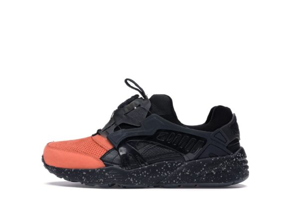 Une sneaker noire et orange avec semelle mouchetée isolée sur fond blanc.